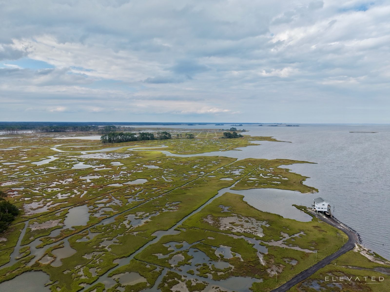 Salt marsh channels running out to open bay, with a lone white house on the shoreline