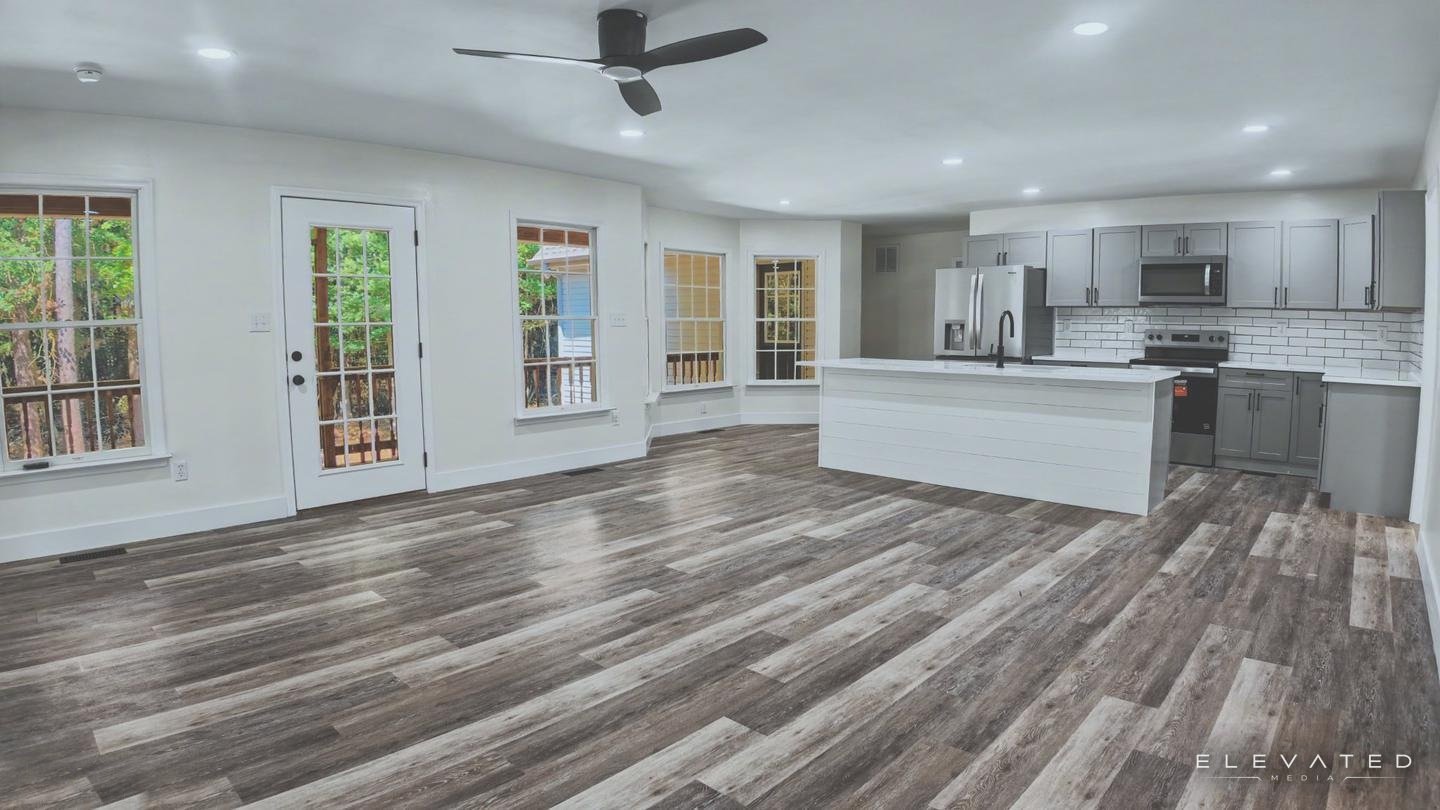 Open living area and gray kitchen with a white shiplap island, wide plank floors, and a wall of windows